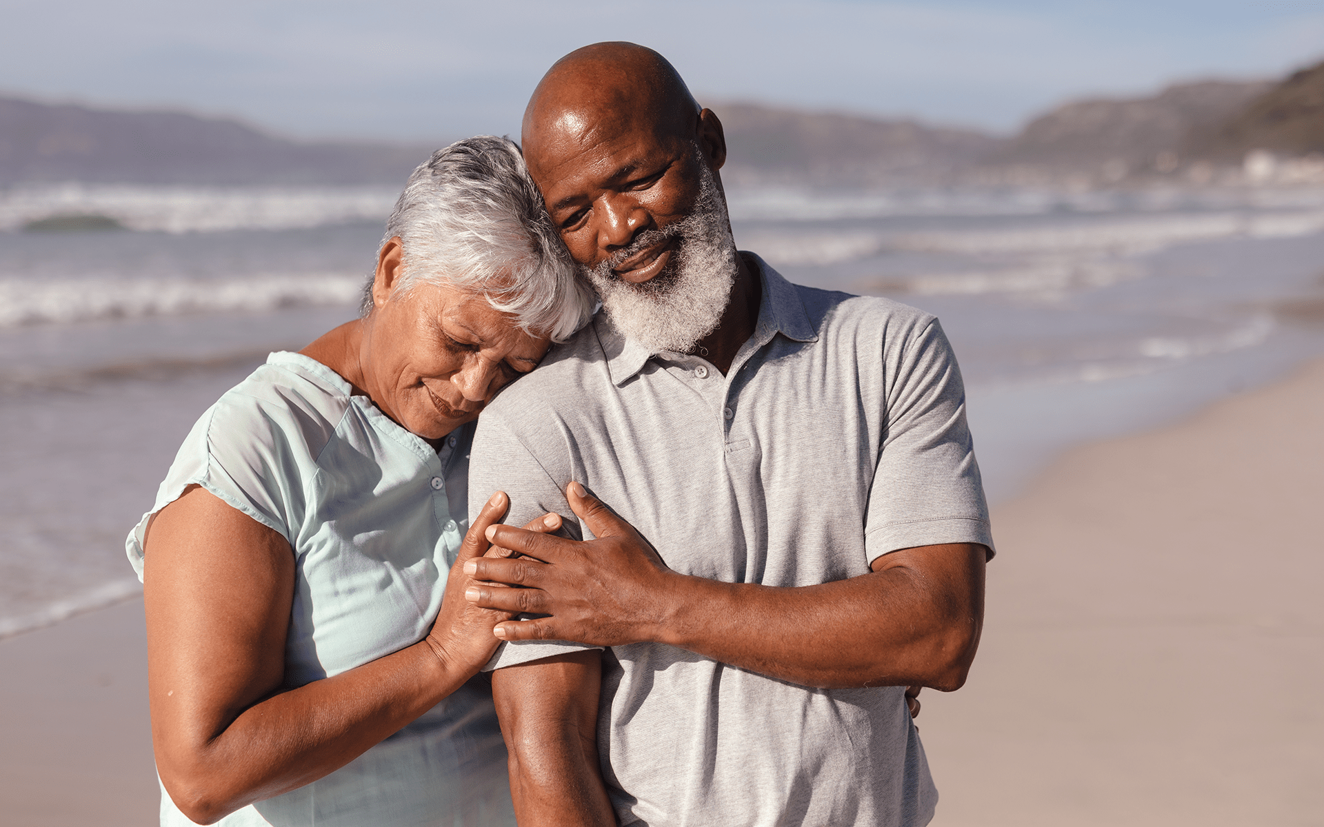 Caregivers, Let's Talk About Caring for Yourself—An elderly Black couple walks along the beach, the wife holder her husband's arm lovingly.